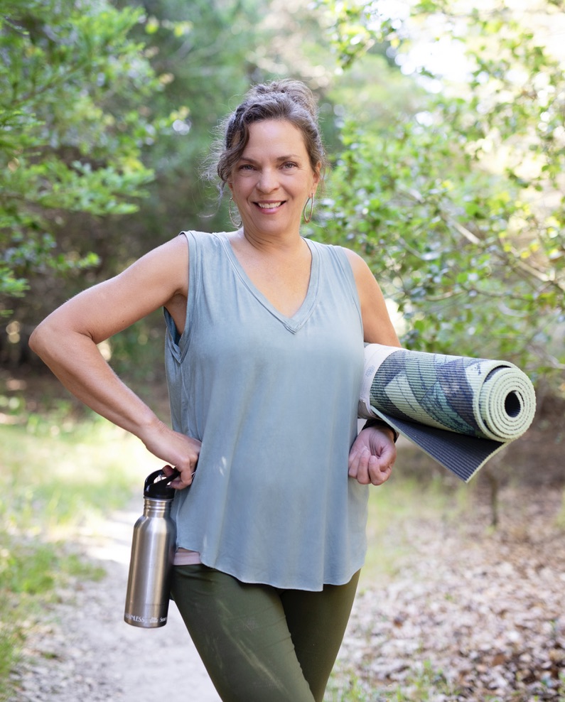 smiling woman holding a yoga mat and a water bottle
